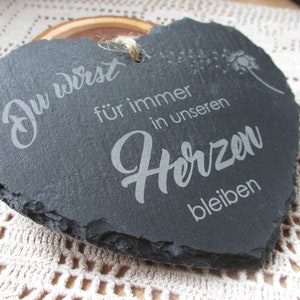K&ouml;nnte beinhalten: Eine schwarze, herzf&ouml;rmige Schiefertafel mit dem Text "Du wirst f&uuml;r immer in unseren Herzen bleiben", der in Wei&szlig; graviert ist. Die Tafel hat einen rauen, nat&uuml;rlichen Rand.