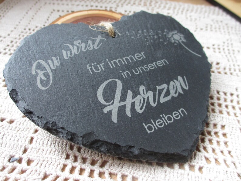 K&ouml;nnte beinhalten: Eine schwarze, herzf&ouml;rmige Schiefertafel mit dem Text "Du wirst f&uuml;r immer in unseren Herzen bleiben", der in Wei&szlig; graviert ist. Die Tafel hat einen rauen, nat&uuml;rlichen Rand.