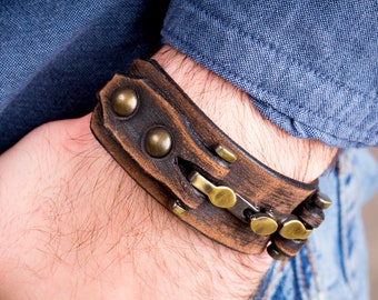 May include: A brown leather bracelet with metal accents. The bracelet has a distressed look and features a chain detail.
