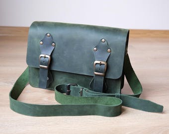 Pode incluir: Uma bolsa de couro verde escura com duas fivelas ajustáveis e uma alça longa. A bolsa tem um fecho de aba e um pequeno bolso na frente.
