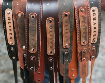 May include: Seven leather camera straps with personalized name tags. The straps are in various shades of brown, black, and tan. The name tags are engraved with the names "Oliver" and "Charles".