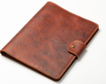 May include: A brown leather binder with a flap closure and a brass button. The binder has a stitched edge and the word "Marlise" embossed on the front.
