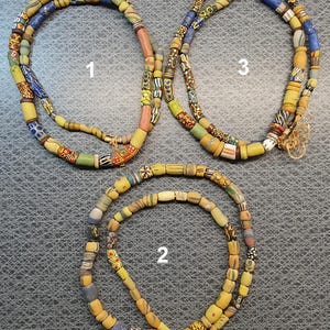 Puede incluir: Tres hileras de collares de cuentas de colores con cuentas amarillas, azules, verdes y rojas. Los collares están numerados del 1 al 3.