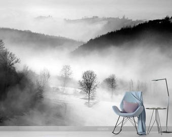 May include: A black and white photograph of a foggy landscape with trees and hills. A blue armchair sits in the foreground, facing the viewer.