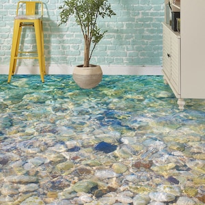 May include: A close-up of a floor with a realistic 3D printed design of a clear blue ocean with rocks and pebbles at the bottom.