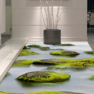 Op de afbeelding: Een 3D-vloermuurdecoratie met een realistische beek met met mos bedekte rotsen en stromend water. Twee hoge witte keramische vazen met zwarte bloemmotieven staan aan de zijkant. Een donkergrijze cilindrische plantenbak staat erachter.