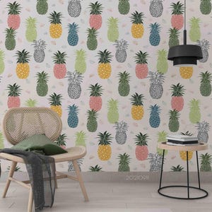 Könnte beinhalten: Tapete mit einem sich wiederholenden Muster aus bunten Ananas in Gelb-, Rosa-, Grün-, Blau- und Schwarztönen. Das Design hat einen hellen Hintergrund und eignet sich für die Inneneinrichtung. Ein Stuhl und ein Beistelltisch befinden sich im Vordergrund.