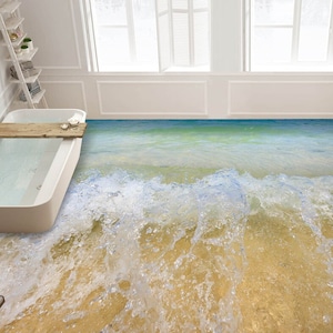 Op de afbeelding: Een wit bad met een houten dienblad staat in een badkamer met een betegelde vloer die eruitziet als een strandscène met blauw water en witte golven.