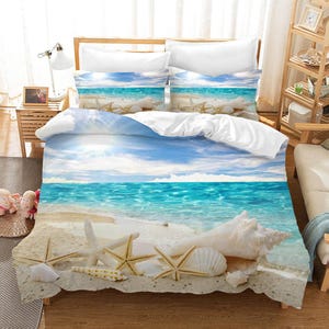 May include: A white and blue beach themed bedding set with a duvet cover featuring a seascape with blue water, white sand, and seashells. The duvet cover has a white and blue striped pattern on the reverse side.