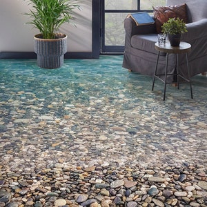 May include: A close-up of a floor with a realistic riverbed design. The floor is covered in smooth, round stones of various sizes and colors, with clear water flowing over them. The floor is a great way to add a touch of nature to any room.