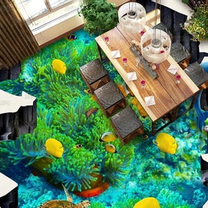 May include: A 3D floor mural featuring a vibrant coral reef scene with bright yellow fish, a sea turtle, and a blue dolphin, set within a cracked white floor design. A wooden dining table with dark square stools is positioned over the underwater imagery.