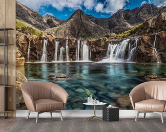 May include: A scenic landscape photograph featuring a waterfall cascading into a clear blue pool of water. The waterfall is surrounded by rocky cliffs and lush green vegetation. The sky is a bright blue with fluffy white clouds.