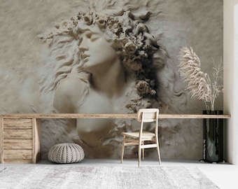 May include: A white plaster bas-relief sculpture of a woman's head with flowers in her hair, set against a textured wall. The sculpture is displayed in a room with a wooden desk, a chair, and a round pouf.