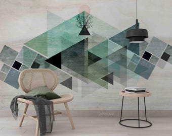 May include: Abstract geometric wall art with overlapping triangles in green, grey, and black. A tree silhouette sits atop a black triangle. A wooden chair with a green cushion and a small side table with books are in the foreground.