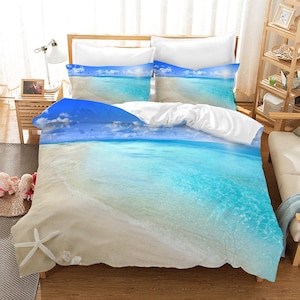 May include: A white and blue beach themed bedding set with a duvet cover featuring a photo of a tropical beach with blue water and white sand. The duvet cover has a starfish design on the bottom.