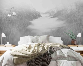 May include: A white bed with a white and gray striped blanket and a beige throw blanket. The bed is in front of a wall with a black and white photo of a mountain range with fog.