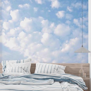 Puede incluir: Una habitación con un mural de cielo azul y nubes sobre una cama con ropa de cama a rayas. La cama tiene almohadas blancas con rayas azules y una cabecera de madera. Una lámpara colgante cuelga del techo.