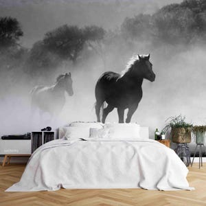 May include: Monochrome mural depicting two horses in a misty environment. The horses are silhouetted against a backdrop of trees and fog. The mural is installed above a bed with white bedding.