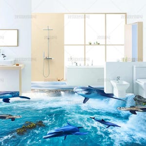May include: A bathroom interior featuring a 3D floor mural of a blue ocean scene with dolphins and a sea turtle swimming in clear water near a waterfall. The room includes a white vanity, a toilet, a bidet, and a bathtub against a wall.