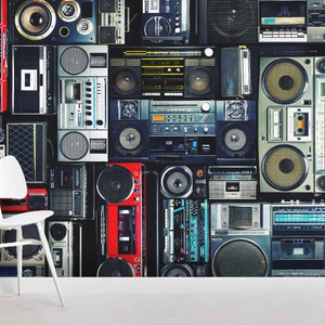 May include: A wall covered in a collage of vintage cassette players and boomboxes in various colors and styles. The players are arranged in a grid pattern, with some overlapping. The wall is a dark gray color.