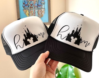 Puede incluir: Dos gorras de camionero blancas y negras con una silueta negra del castillo de Cenicienta y el texto "home" en cada gorra.