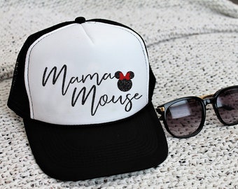 Puede incluir: Una gorra de camionero blanca y negra con el texto "Mama Mouse" en escritura negra y una silueta de Minnie Mouse negra y roja de purpurina.