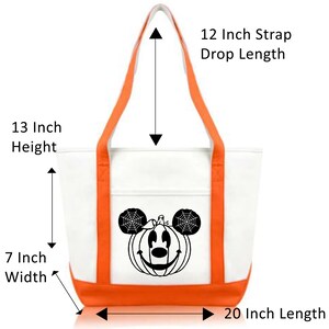 K&ouml;nnte beinhalten: Wei&szlig;e Canvas-Tragetasche mit orangefarbenem Besatz und einem schwarzen K&uuml;rbis-Mickey-Mouse-Design. Die Tasche ist 33 cm hoch, 18 cm breit und 51 cm lang. Die L&auml;nge des Trageriemens betr&auml;gt 30 cm.