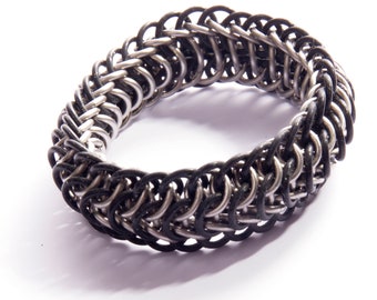 May include: A black and silver chainmail bracelet with a woven design.