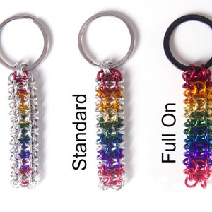 May include: Three keychains with rainbow-colored chainmaille accents. The keychains are attached to silver rings. The first keychain is labeled "Subtle", the second "Standard", and the third "Full On". The keychains are on a white background.