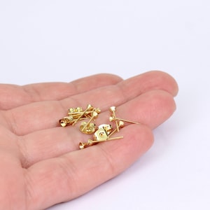 May include: Several small, gold-colored earring posts and backs are displayed. The posts have a simple, rounded design, while the backs feature a butterfly clasp. The earrings are shown against a neutral background.