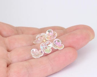 May include: A collection of small, translucent flower-shaped beads with an iridescent finish. Each bead features five rounded petals and a central hole for threading, displaying subtle rainbow reflections across the clear, glossy surface.