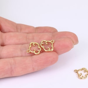 May include: Two gold-colored cloud-shaped charms with small loops for attaching to jewelry. The charms are held in a hand against a white background. The charms have a glossy finish and a delicate, open design.