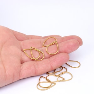 May include: Gold-coloured teardrop-shaped jewellery findings. The open-frame teardrops are arranged in a hand against a white background. These findings are suitable for creating earrings, pendants, or other jewellery designs.