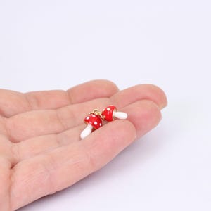 May include: Two red and white mushroom charms with gold accents. The charms are hanging from a gold chain.