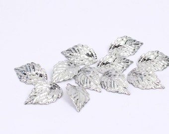 May include: A group of silver metal leaves, scattered on a white surface. The leaves have a textured, slightly raised design.