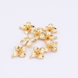 May include: A group of eight gold-coloured metal flower charms with a loop on the back for attaching to jewellery or other crafts.
