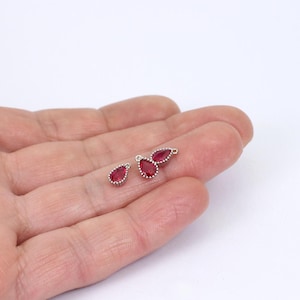May include: Three silver teardrop charms with red crystal accents. The charms have a loop at the top for attaching to jewellery.