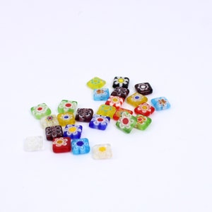 May include: Assortment of colourful square glass beads with floral designs. The beads are translucent and have a variety of colours, including red, blue, green, yellow, and purple.