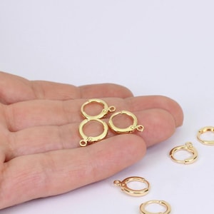 May include: A collection of gold-coloured leverback earring findings. The findings are circular with a small loop at the bottom for attaching charms or beads. The earrings are shown against a white background.