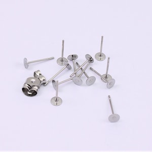 May include: A close-up of a pile of silver earring posts with flat backs. The posts are made of metal and have a shiny finish.