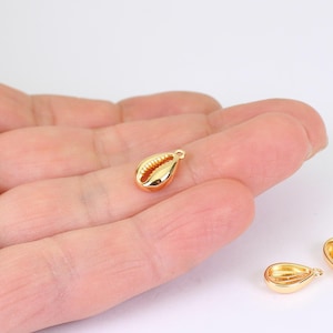 May include: A small, gold-coloured seashell charm with a loop at the top for jewellery making. The charm has a detailed, textured surface and a polished, reflective finish. The charm is approximately 1.3 cm long.