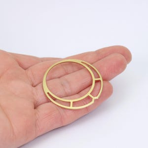 以下が含まれることがあります： 幾何学模様の金色の金属製のリング。リングは片側が開いており、円形をしています。
