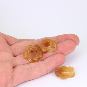 May include: Three translucent, flower-shaped beads in shades of amber and brown. Each bead has a central hole and rounded petals. The beads are displayed against a white background.