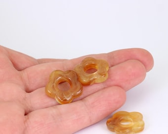 May include: Three translucent, flower-shaped beads in shades of amber and brown. Each bead has a central hole and rounded petals. The beads are displayed against a white background.