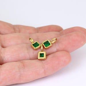May include: Three gold pendants, each featuring a square, emerald-green gemstone. The pendants have a small loop for a chain. The image shows the pendants against a white backdrop.