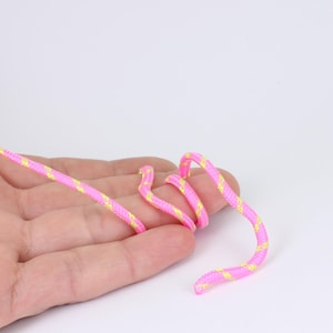 May include: A length of pink and yellow striped rope, coiled in a hand. The rope is a bright pink with yellow diagonal stripes. The background is plain white.
