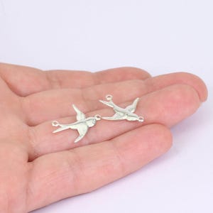 May include: Two silver bird charms in flight. Each charm features a detailed bird silhouette with outstretched wings and a small loop for attaching to jewellery. The charms are displayed against a light background.