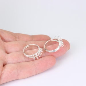 May include: Two silver adjustable rings with a decorative design. The rings are displayed on a light background. The rings have a delicate, openwork design on the top, adding a touch of elegance to the jewellery.