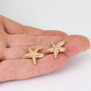 May include: A pair of rose gold-toned starfish-shaped stud earrings. Each earring features a textured, five-pointed surface that mimics the appearance of a natural starfish, with a metallic finish and a small post backing for secure attachment.