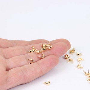 Könnte beinhalten: Nahaufnahme einer Hand, die eine Gruppe von goldfarbenen Metallperlenkappen hält. Die Kappen sind so konzipiert, dass sie als Endkappen für Halsketten, Armbänder oder andere Schmuckprojekte verwendet werden können.